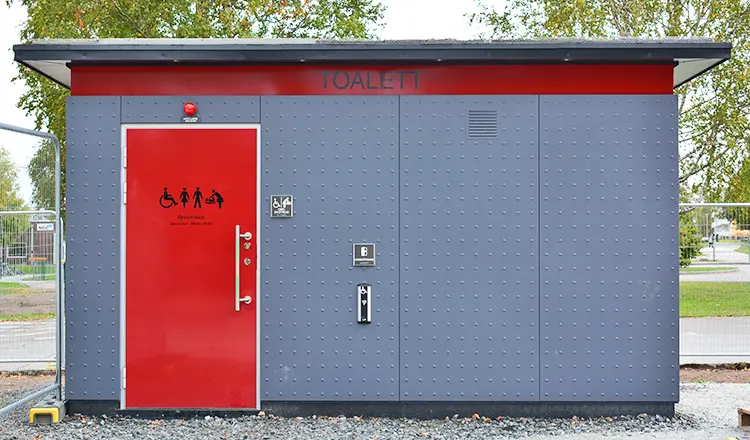  Grå toalettbyggnad med röd dörr