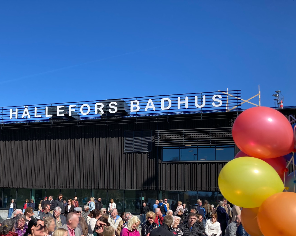 blå himmel, skylt med Hällefors Badhus, ballonger och publik