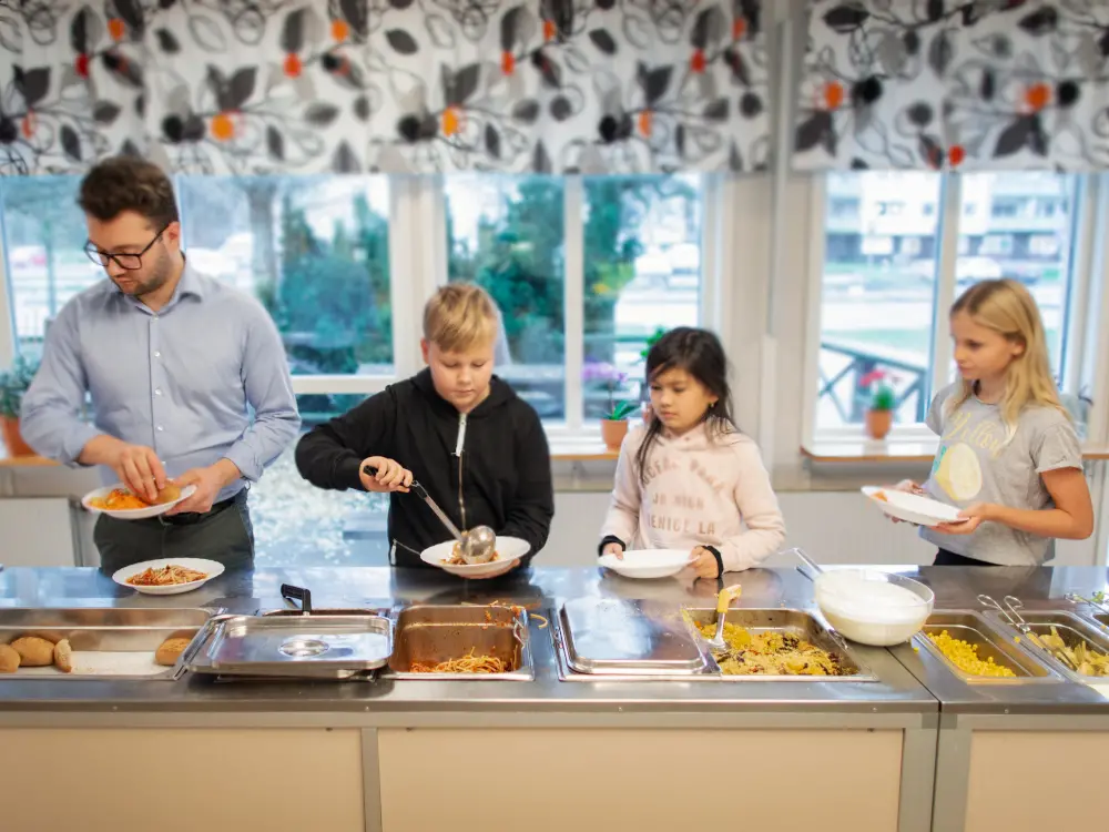 Lärare och barn lägger upp mat på sin tallrik
