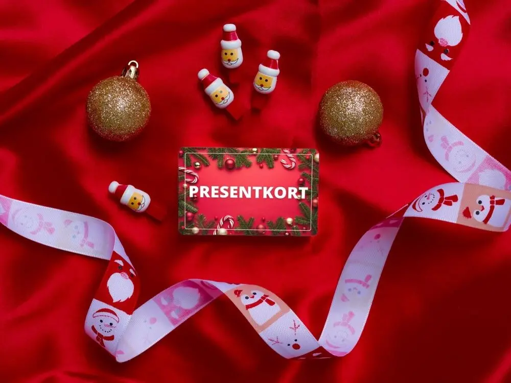 Bild på presentkort liggande på en duk omgiven av julkulor och julsnöre
